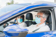 © Tomaspf_ - New normal. Driver with a medical face mask driving a car with a passenger. Health protection. Family in the car protected by a mask safety and pandemic concept. Coronavirus devices. Social distance.