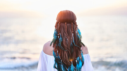 Wall Mural - Serene peaceful tranquil boho hippie woman with blue feathers in hair standing back and looking to sea. Calm and freedom concept