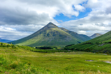 A scenic view of a grassy pyramidal Highland Scottish mountain (Beinn Dòbhrain) with grassy slope under a majestic blue sky and some white clouds