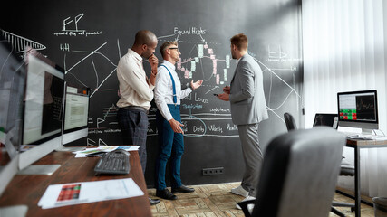 Wall Mural - The best learning environment. Full-length shot of diverse employees, traders standing near blackboard full of charts, while discussing the strategy of work. Horizontal shot