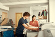 © Svitlana - We customize literally anything. Young workers, man and woman are preparing t-shirt for printing in the silk screen printing machine at workplace
