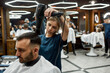© Svitlana - Modern barbershop. Young bearded handsome man sitting in barbershop chair while female barber drying his hair. Getting hairut. Selective focus