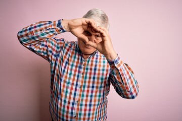 Wall Mural - Senior handsome hoary man wearing casual colorful shirt over isolated pink background Doing heart shape with hand and fingers smiling looking through sign