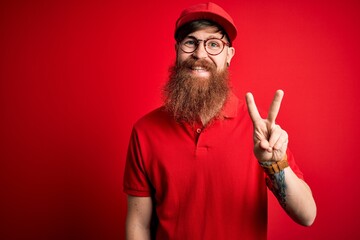 Canvas Print - Young handsome delivery man wearing glasses and red cap over isolated background showing and pointing up with fingers number two while smiling confident and happy.