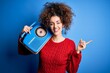 © Krakenimages.com - Young beautiful woman with curly hair and piercing listening to music using vintage radio very happy pointing with hand and finger to the side