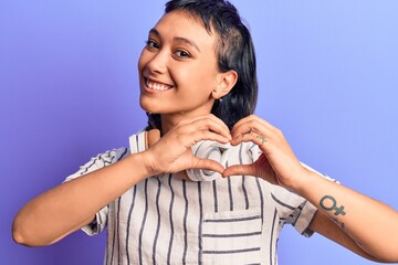 Wall Mural - Young woman listening to music using headphones smiling in love doing heart symbol shape with hands. romantic concept.