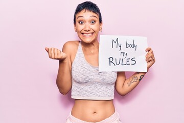 Young woman holding my body my rules banner screaming proud, celebrating victory and success very excited with raised arm