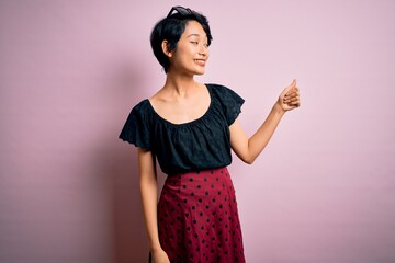 Wall Mural - Young beautiful asian girl wearing casual dress standing over isolated pink background Looking proud, smiling doing thumbs up gesture to the side