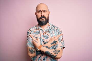 Wall Mural - Handsome bald man with beard and tattoo wearing casual floral shirt over pink background Pointing to both sides with fingers, different direction disagree