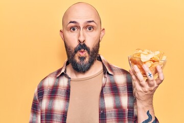 Sticker - Young handsome man holding potato chip scared and amazed with open mouth for surprise, disbelief face