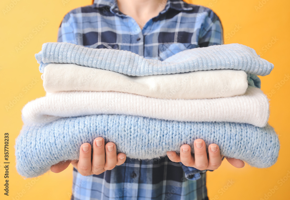 Woman with stack of clean clothes on color background, closeup