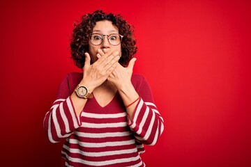 Sticker - Middle age beautiful curly hair woman wearing casual striped sweater over red background shocked covering mouth with hands for mistake. Secret concept.