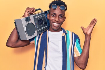 Young african american man holding boombox, listening to music celebrating victory with happy smile and winner expression with raised hands