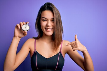 Wall Mural - Young beautiful sporty girl doing sport using stopwatch over isolated purple background with surprise face pointing finger to himself