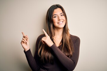 Sticker - Young beautiful girl wearing casual sweater standing over isolated white background smiling and looking at the camera pointing with two hands and fingers to the side.