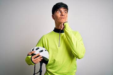 Poster - Young handsome cyclist man holding security bike helmet over isolated white background serious face thinking about question, very confused idea