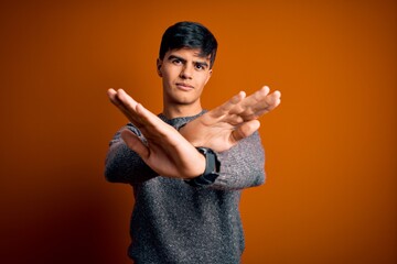 Sticker - Young handsome man wearing casual sweater standing over isolated orange background Rejection expression crossing arms and palms doing negative sign, angry face