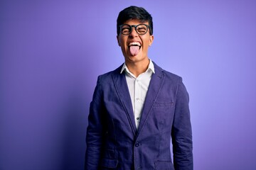 Canvas Print - Young handsome business man wearing jacket and glasses over isolated purple background sticking tongue out happy with funny expression. Emotion concept.