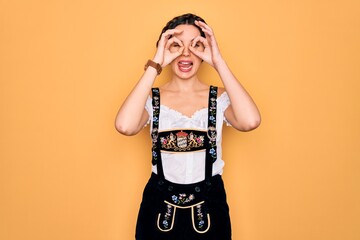 Wall Mural - Young beautiful german woman with blue eyes wearing traditional octoberfest dress doing ok gesture like binoculars sticking tongue out, eyes looking through fingers. Crazy expression.