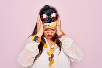 Wall Mural - Young hispanic hippie woman wearing fashion boho style and sunglasses over pink background suffering from headache desperate and stressed because pain and migraine. Hands on head.