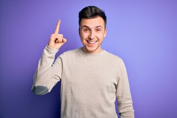 Wall Mural - Young handsome caucasian man wearing casual sweater over purple isolated background pointing finger up with successful idea. Exited and happy. Number one.