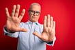© Krakenimages.com - Middle age handsome hoary man wearing casual striped shirt and glasses over red background doing frame using hands palms and fingers, camera perspective
