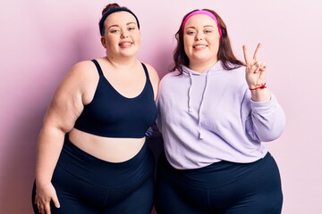 Young plus size twins wearing sportswear showing and pointing up with fingers number two while smiling confident and happy.