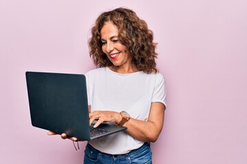 Middle age beautiful business woman working using laptop over isolated pink background looking positive and happy standing and smiling with a confident smile showing teeth