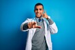 © Krakenimages.com - Handsome african american doctor man wearing coat and stethoscope over blue background smiling doing talking on the telephone gesture and pointing to you. Call me.