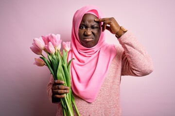 Canvas Print - Young african american plus size woman wearing muslim hijab holding bouquet of pink tulips worried and stressed about a problem with hand on forehead, nervous and anxious for crisis