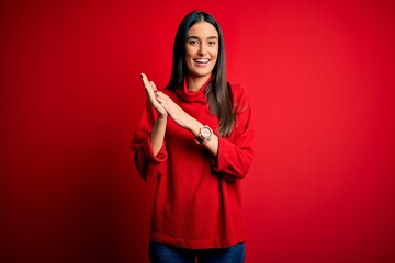 Young beautiful brunette woman wearing casual sweater over isolated red background clapping and applauding happy and joyful, smiling proud hands together