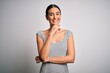 © Krakenimages.com - Young beautiful brunette woman wearing casual striped dress over isolated white background looking confident at the camera smiling with crossed arms and hand raised on chin. Thinking positive.