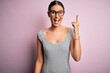 © Krakenimages.com - Young beautiful woman wearing casual striped dress and glasses over pink background pointing finger up with successful idea. Exited and happy. Number one.