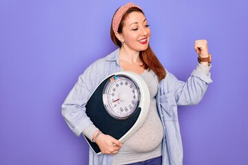 Sticker - Young beautiful redhead pregnant woman expecting baby holding weighting machine pointing and showing with thumb up to the side with happy face smiling