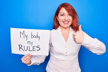 Sticker - Young redhead woman asking for women rights holding paper with my body my rules message smiling happy and positive, thumb up doing excellent and approval sign