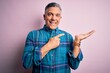 © Krakenimages.com - Middle age handsome grey-haired man wearing casual shirt over isolated pink background amazed and smiling to the camera while presenting with hand and pointing with finger.