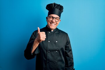 Sticker - Middle age handsome grey-haired chef man wearing cooker uniform and hat doing happy thumbs up gesture with hand. Approving expression looking at the camera showing success.