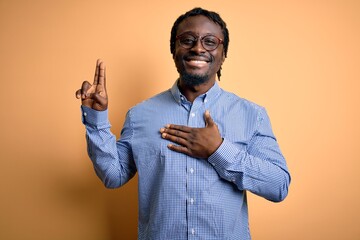 Poster - Young handsome african american man wearing shirt and glasses over yellow background smiling swearing with hand on chest and fingers up, making a loyalty promise oath