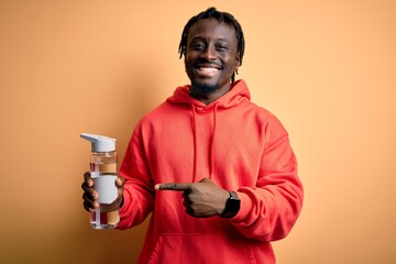 Canvas Print - Young african american sporty man wearing sweatshirt with hoodie drinking bottle of water very happy pointing with hand and finger