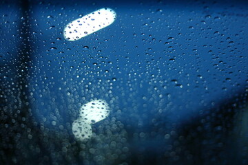 Wall Mural - water rain drop on glass window with blur street light in night town background