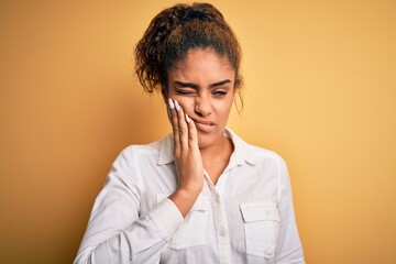 Poster - Young beautiful african american girl wearing casual shirt standing over yellow background touching mouth with hand with painful expression because of toothache or dental illness on teeth. Dentist