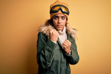 Wall Mural - Young african american afro skier girl wearing snow sportswear and ski goggles Ready to fight with fist defense gesture, angry and upset face, afraid of problem