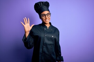 Poster - Young african american chef girl wearing cooker uniform and hat over purple background showing and pointing up with fingers number five while smiling confident and happy.