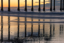 Pier Posts Reflecting On Wet Sand During Sunset.