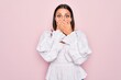 © Krakenimages.com - Young beautiful brunette woman wearing casual white dress standing over pink background shocked covering mouth with hands for mistake. Secret concept.