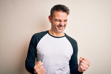 Young handsome man wearing casual t-shirt standing over isolated white background excited for success with arms raised and eyes closed celebrating victory smiling. Winner concept.