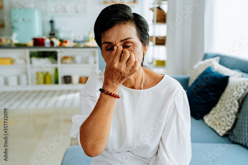 Fotografía Mature Asian lady with closed eyes rubbing nose while sitting on sofa and suffer