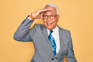 Poster - Middle age senior grey-haired handsome business man wearing glasses over yellow background very happy and smiling looking far away with hand over head. Searching concept.