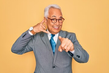 Canvas Print - Middle age senior grey-haired handsome business man wearing glasses over yellow background smiling doing talking on the telephone gesture and pointing to you. Call me.