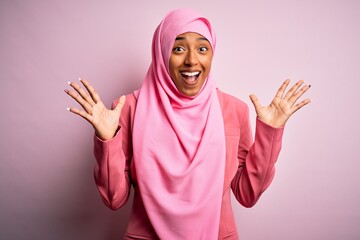 Young African American afro woman wearing muslim hijab over isolated pink background celebrating crazy and amazed for success with arms raised and open eyes screaming excited. Winner concept